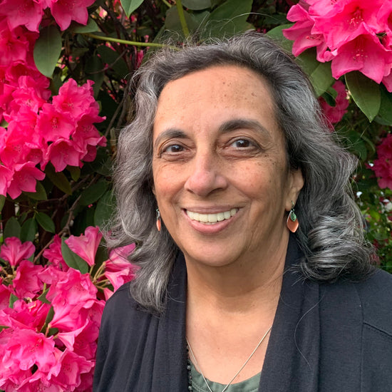Woman with gray hair smiling in front of pink flowers