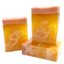Three rectangular bars of handcrafted leo soap in shades of orange and yellow with white text, packaged in clear plastic sleeves, on a white background. Vanilla vanity scented, smells like its all about you