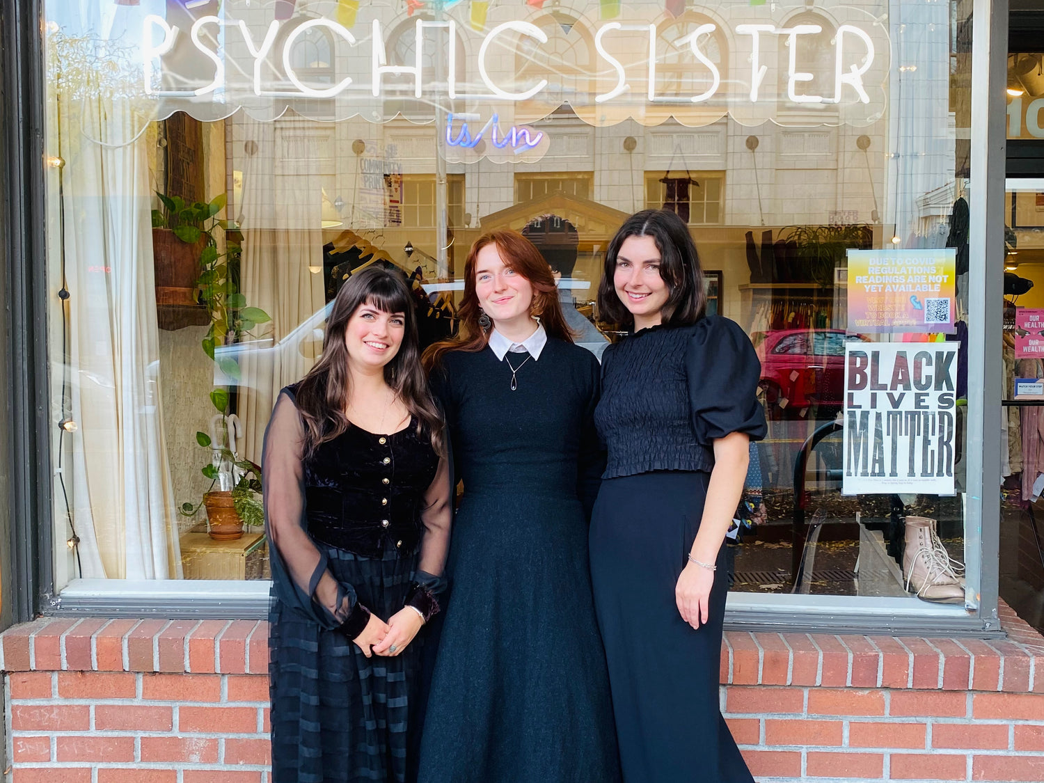 Three employees standing in front of the Psychic Sister shop window.