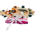 Pink package with a white ribbon surrounded by colorful stones on a white background