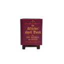 A miniature book-shaped desk candle or holder reading 'the Witches' Spell Book for LOVE, HAPPINESS, and SUCCESS' in gold lettering, displayed on a small wooden stand against a white background.