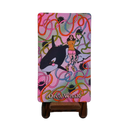 A rectangular product with rounded corners, standing on a small brown base, featuring a colorful retro-style illustration of an orca whale and a woman on a pink background with swirling multicolored lines. The words 'Orca Whale' appear near the bottom.