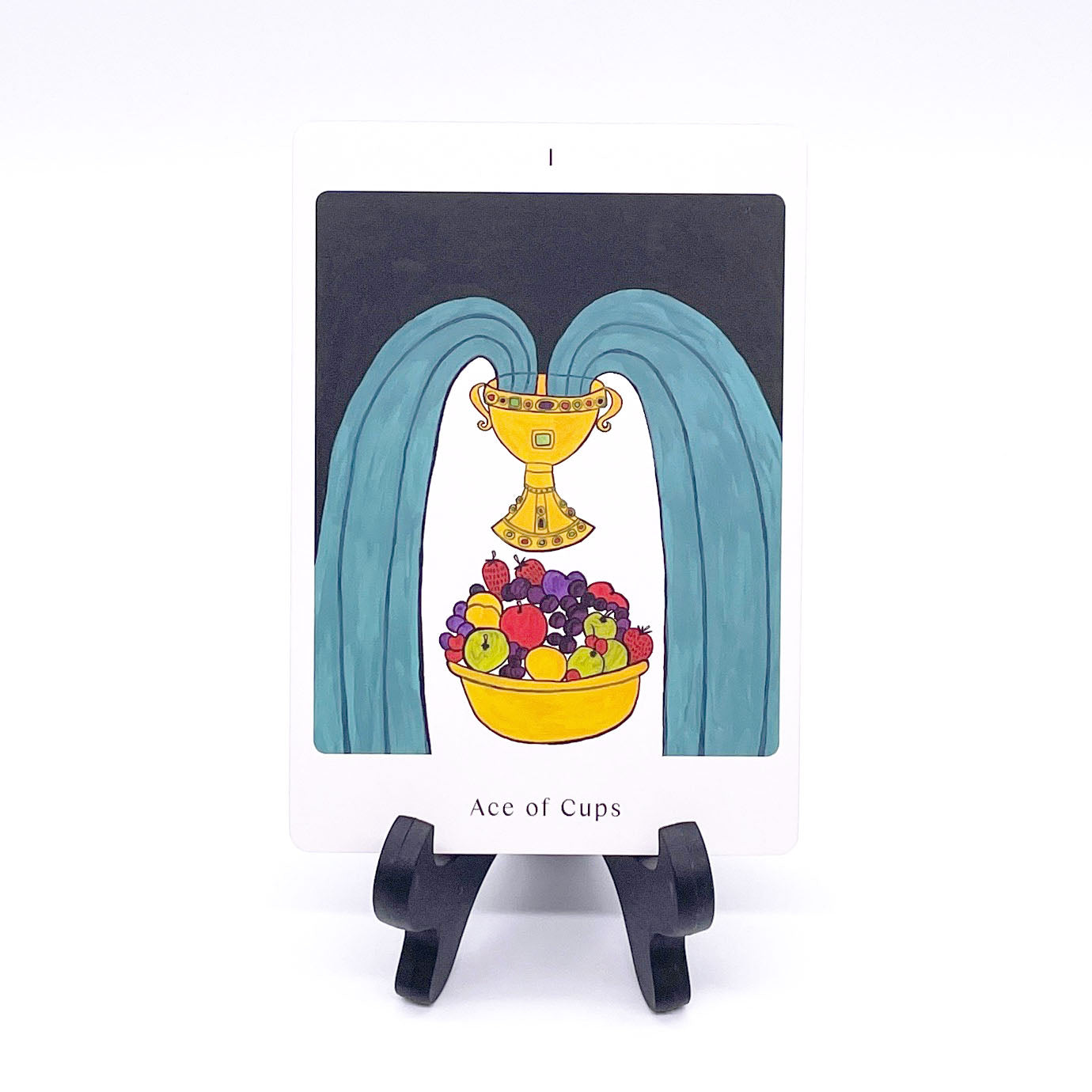 Ace of Cups card showing a fountain of teal water pouring from a golden goblet hovering over a bowl filled with brightly colored fruit. Card is printed with the title and corresponding number "I".