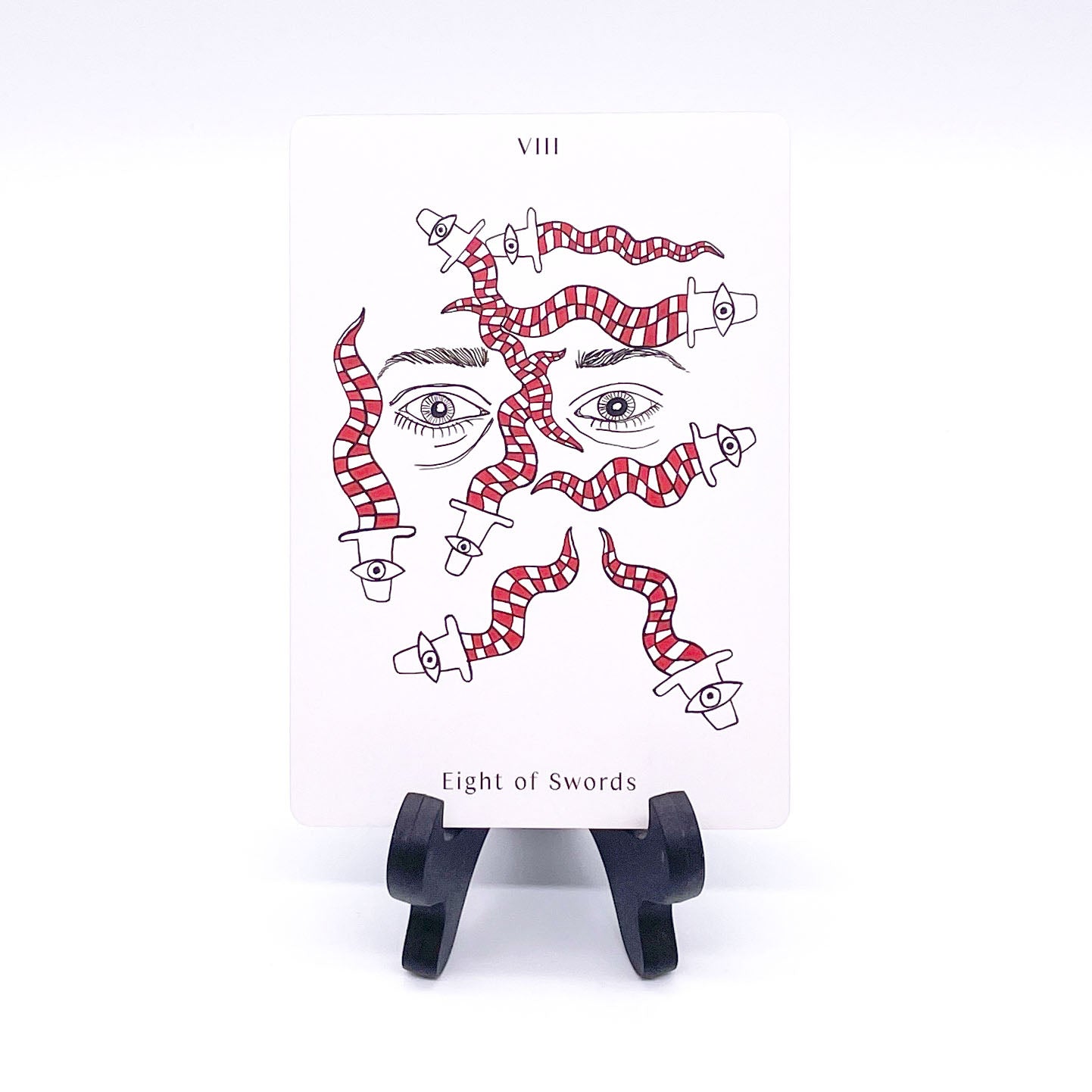 Eight of Swords card showing wavy red and white checkered swords with eyes on the hilts, set over a pair of floating eyes with eyebrows above and bags underneath them. Card is printed with the title and corresponding number "VIII".