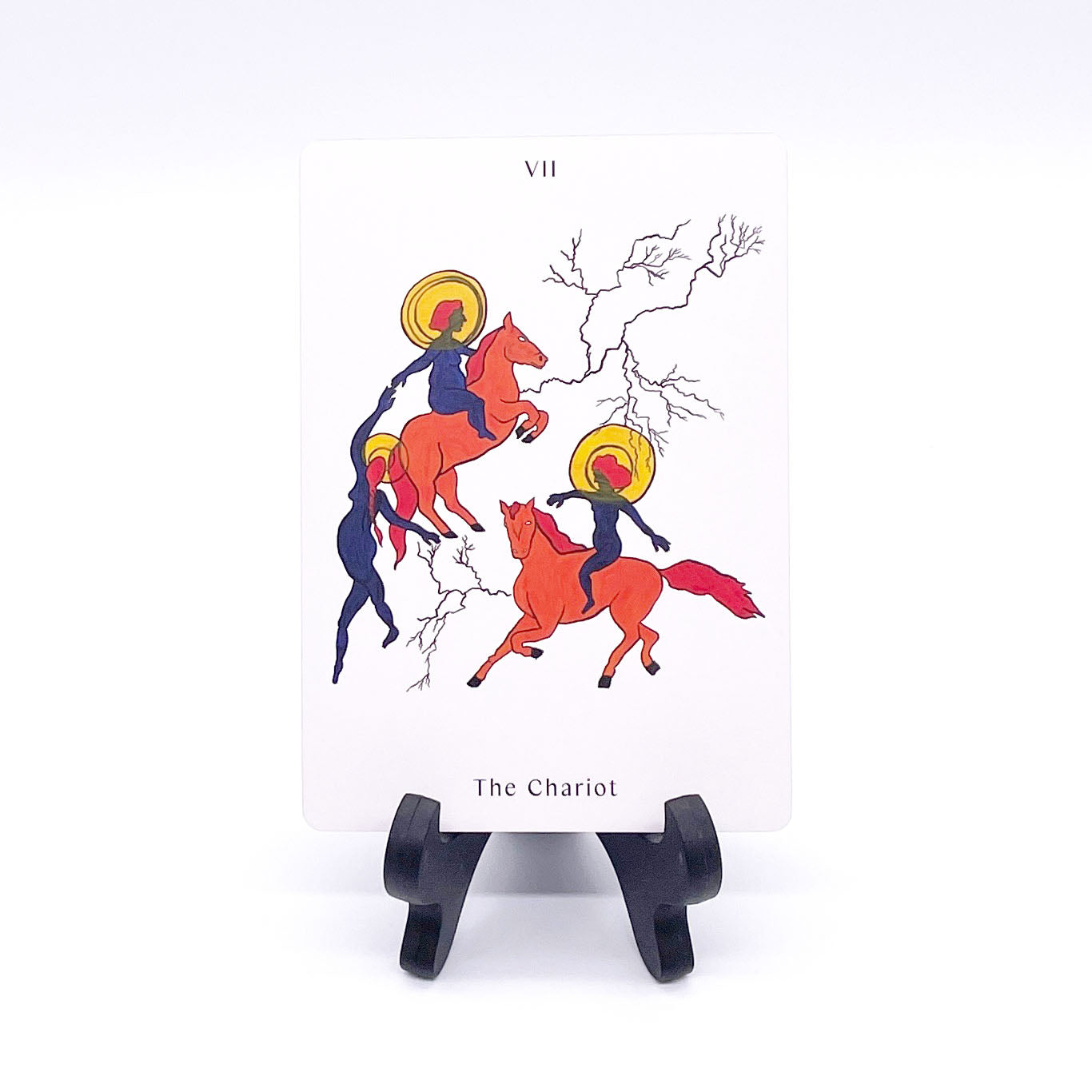 The Chariot card showing three femme figures in navy blue--two are riders on orange horses and all three have golden halos around their heads. They are connected by branching lines. Card is printed with the title and corresponding Major Arcana number "VII"