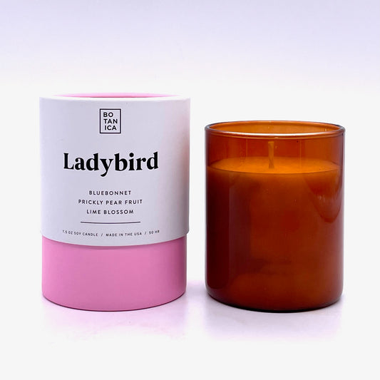 Amber Glass Candle next to White & Pink Tube Package with Black Text