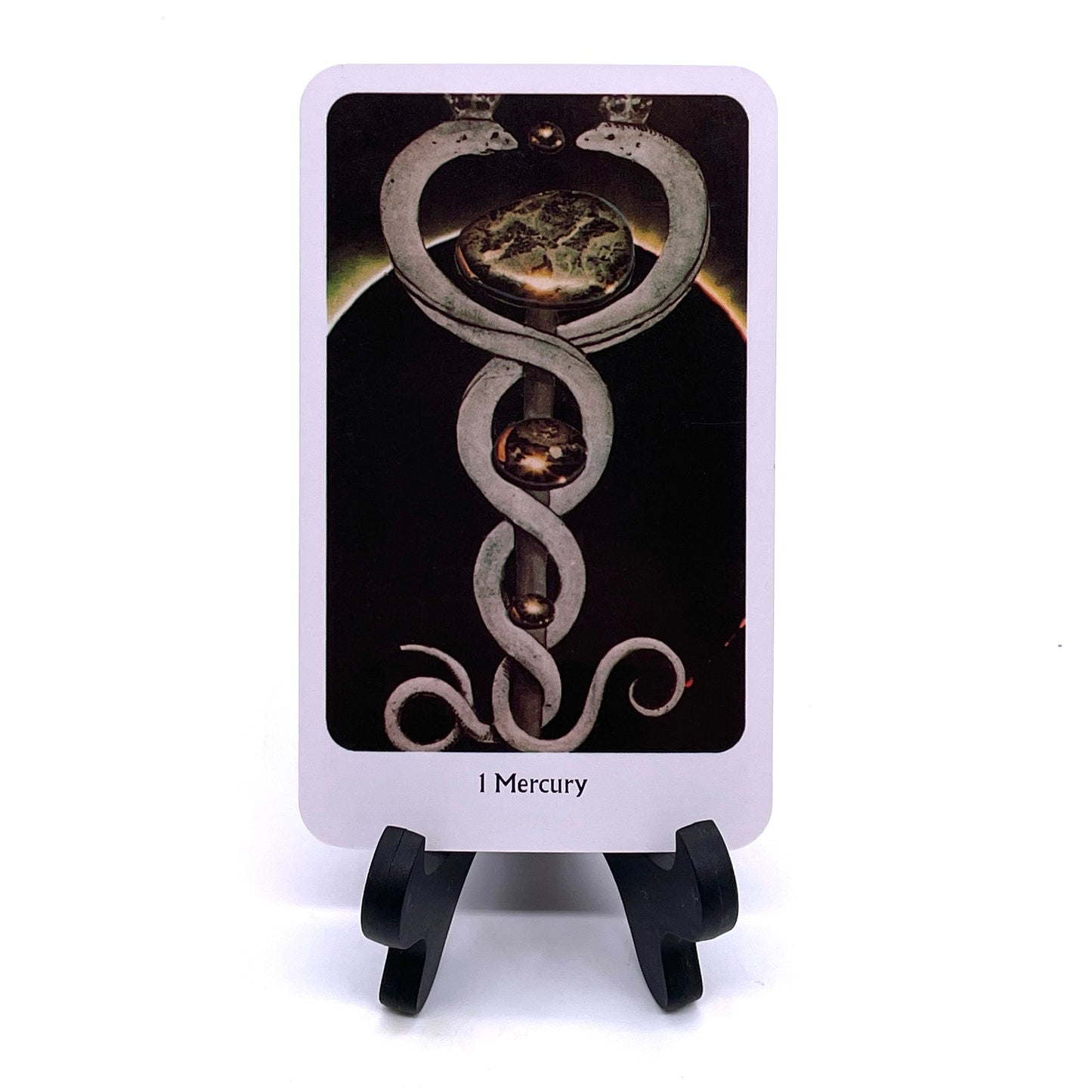 Photo of Card #1 "Mercury", featuring collaged images of two serpents facing each other and wrapped symmetrically around a scepter in front of a solar eclipse background.