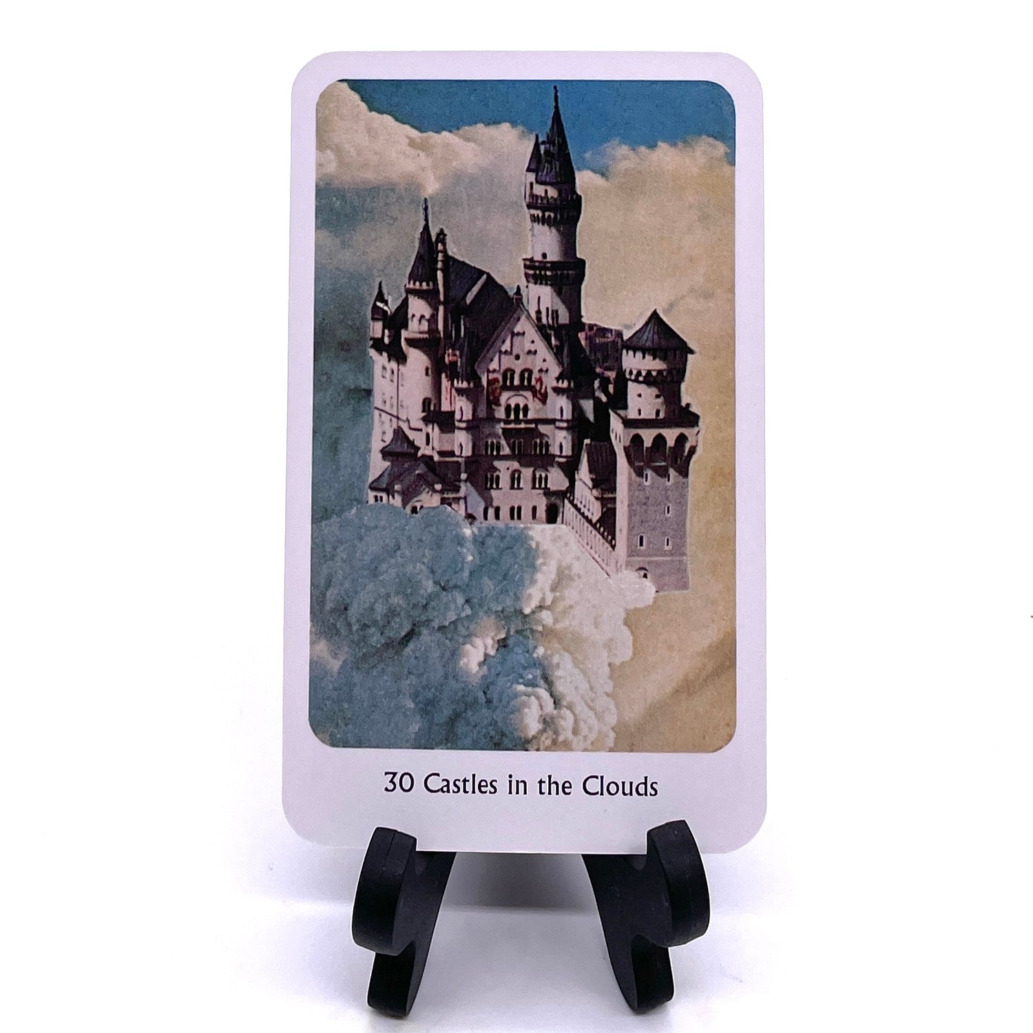 Photo of Card #30, "Castles in the Clouds", featuring collaged images of a white castle with back roofs against fluffy white clouds.