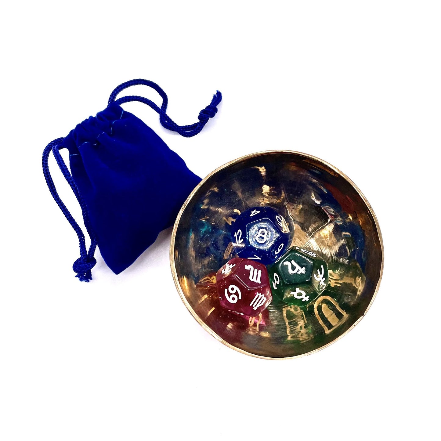 Three astro dice inside a gold bowl next to a blue velvet pouch.