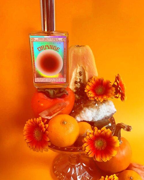 Moon Nectar Vibrational color spray in orange displayed with flowers and crystals.